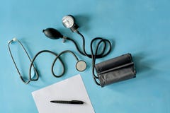 Papel branco da folha com o estetoscópio preto da pena e do phonendoscope, sphygmomanometer no fundo azul fotografia de stock royalty free Papel branco da folha com o estetoscópio preto da pena e do phonendoscope, sphygmomanometer no fundo azul fotografia de stock royalty free