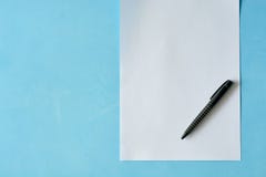 Papel branco da folha com a pena preta isoleted no claro - fundo azul fotografia de stock Papel branco da folha com a pena preta isoleted no claro - fundo azul fotografia de stock
