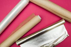 Papier d'aluminium d'enveloppe et en plastique et rouleau de papier parcheminé sur le fond rose image stock Papier d'aluminium d'enveloppe et en plastique et rouleau de papier parcheminé sur le fond rose image stock