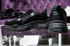Para czarni sneakers na tle szk?o st?? i purpurowa kanapa zdjęcie royalty free Para czarni sneakers na tle szk?o st?? i purpurowa kanapa zdjęcie royalty free