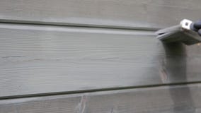 Pared exterior de la casa de madera de la pintura del trabajador de mujer con la brocha y el color protector de madera almacen de metraje de vídeo Pared exterior de la casa de madera de la pintura del trabajador de mujer con la brocha y el color protector de madera almacen de metraje de vídeo