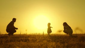 Parents are taught to walk a small child, little girl makes her first steps in sun, slow motion. parents play with their