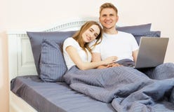 Pares adolescentes felices usando el ordenador portátil en cama en el dormitorio Pareja de matrimonios joven que miente en cama e imágenes de archivo libres de regalías Pares adolescentes felices usando el ordenador portátil en cama en el dormitorio Pareja de matrimonios joven que miente en cama e imágenes de archivo libres de regalías