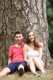 Pares adolescentes novos que sentam-se contra uma árvore fotos de stock Pares adolescentes novos que sentam-se contra uma árvore fotos de stock