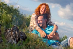 Pares atractivos de la sonrisa cariñosa feliz que ponen por la hoguera que abraza en hierba y nubes El par ama los relojes casual imagenes de archivo Pares atractivos de la sonrisa cariñosa feliz que ponen por la hoguera que abraza en hierba y nubes El par ama los relojes casual imagenes de archivo