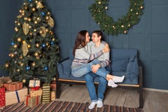 Pares atrativos que sentam-se em um sofá que abraça maciamente com uma árvore de Natal no fundo imagens de stock Pares atrativos que sentam-se em um sofá que abraça maciamente com uma árvore de Natal no fundo imagens de stock