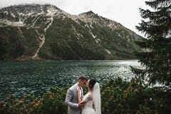 Pares de la boda que se besan cerca del lago en las monta?as de Tatra en Polonia Morskie Oko D?a de verano hermoso imagenes de archivo Pares de la boda que se besan cerca del lago en las monta?as de Tatra en Polonia Morskie Oko D?a de verano hermoso imagenes de archivo