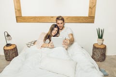 Pares del individuo y de la muchacha en cama que miran una tableta fotografía de archivo Pares del individuo y de la muchacha en cama que miran una tableta fotografía de archivo
