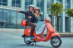 Pares felices atractivos, un hombre hermoso y el montar femenino atractivo junto en una vespa retra roja en una ciudad foto de archivo libre de regalías Pares felices atractivos, un hombre hermoso y el montar femenino atractivo junto en una vespa retra roja en una ciudad foto de archivo libre de regalías