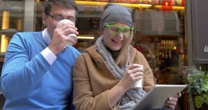 Pares felices usando la tableta de Digitaces en el café de la calle metrajes Pares felices usando la tableta de Digitaces en el café de la calle metrajes