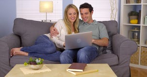 Pares felizes usando o portátil no sofá imagem de stock Pares felizes usando o portátil no sofá imagem de stock