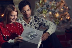 Pares jovenes que abren un regalo de Navidad Fotos de archivo Pares jovenes que abren un regalo de Navidad Fotos de archivo