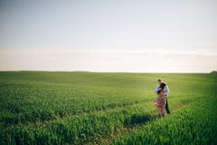 Pares novos bonitos que abraçam delicadamente na luz do sol no campo do verde da mola Família feliz que abraça no prado verde com foto de stock Pares novos bonitos que abraçam delicadamente na luz do sol no campo do verde da mola Família feliz que abraça no prado verde com foto de stock