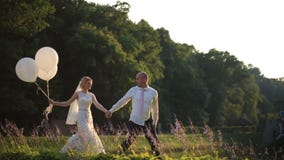 Pares novos felizes do casamento que andam com ballooons no campo do verão no por do sol Conceito romântico do casamento filme Pares novos felizes do casamento que andam com ballooons no campo do verão no por do sol Conceito romântico do casamento filme