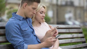 Pares novos que sentam-se no banco e que usam telefones celulares, rede social, distração filme Pares novos que sentam-se no banco e que usam telefones celulares, rede social, distração filme