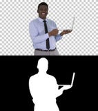 Parlant au jeune homme africain de caméra avec l'ordinateur portable dans des ses mains, Alpha Channel photographie stock libre de droits Parlant au jeune homme africain de caméra avec l'ordinateur portable dans des ses mains, Alpha Channel photographie stock libre de droits