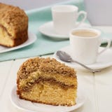 Parte do close-up de bolo de café caseiro do crumble da canela e de copo do chá do leite Fundo de madeira branco quadrado fotos de stock royalty free Parte do close-up de bolo de café caseiro do crumble da canela e de copo do chá do leite Fundo de madeira branco quadrado fotos de stock royalty free