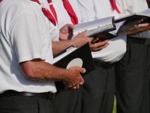 Partial view of 3 singers of a choir, holding in their hands textbooks, dark trousers, white short-sleeved shirt, red kerchief stock image Partial view of 3 singers of a choir, holding in their hands textbooks, dark trousers, white short-sleeved shirt, red kerchief stock image