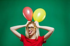 Party Girl in Fashionable Glasses is Grimacing and Looking at the Camera Holding Yellow and Red Air Balloons in the stock image Party Girl in Fashionable Glasses is Grimacing and Looking at the Camera Holding Yellow and Red Air Balloons in the stock image