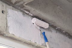 Peignez le rouleau et l'amorce sur le mur au-dessus de la fenêtre Concept de réparer des maisons, appartements, préparant des mur photographie stock libre de droits Peignez le rouleau et l'amorce sur le mur au-dessus de la fenêtre Concept de réparer des maisons, appartements, préparant des mur photographie stock libre de droits