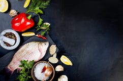 Peixes crus e ingredientes para cozinhar no fundo escuro Imagens de Stock Peixes crus e ingredientes para cozinhar no fundo escuro Imagens de Stock