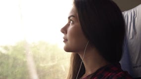 Pensive girl travels by train. Sitting next to the window. Looking up. Listen music in earphones. Thoughtful look. Side