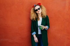 People and leisure concept. Horizontal portrait of pretty girl wearing headband, jacket, jeans and sunglasses holding cup of hot d stock image People and leisure concept. Horizontal portrait of pretty girl wearing headband, jacket, jeans and sunglasses holding cup of hot d stock image