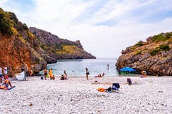 People resting on amazing Cala Bianca beach surrounded by rocks and Tyrrhenian sea bay with crystal clear deep water full of