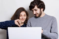 People, technology and communication concept. Stylish bearded guy and his girlfriend using laptop and browsing internet for online Stock Images People, technology and communication concept. Stylish bearded guy and his girlfriend using laptop and browsing internet for online Stock Images