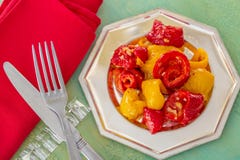 Peperoni dolci fritti gialli rossi cucinati su un piatto d'argento Forcella e coltello e tovagliolo rosso Vecchia tabella immagine stock libera da diritti Peperoni dolci fritti gialli rossi cucinati su un piatto d'argento Forcella e coltello e tovagliolo rosso Vecchia tabella immagine stock libera da diritti