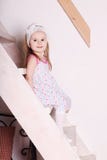 Pequeña muchacha sonriente rubia en el vestido que se sienta en las escaleras de madera Imágenes de archivo libres de regalías Pequeña muchacha sonriente rubia en el vestido que se sienta en las escaleras de madera Imágenes de archivo libres de regalías