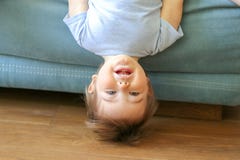 Pequeño colgante divertido lindo del bebé al revés en el sofá que mira la cámara, sonriendo foto de archivo libre de regalías Pequeño colgante divertido lindo del bebé al revés en el sofá que mira la cámara, sonriendo foto de archivo libre de regalías