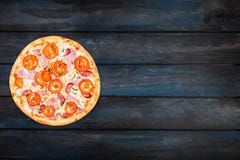 Perfect classic pizza with ham, mushrooms and tomatoes on a dark background. Top view orientation on the left side royalty free stock photo Perfect classic pizza with ham, mushrooms and tomatoes on a dark background. Top view orientation on the left side royalty free stock photo