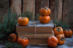 Persimmon on the pack of old books on the wooden background with branches of fir tree