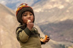 A Peruvian boy in a warm hat eats a tangerine while looking at the camera