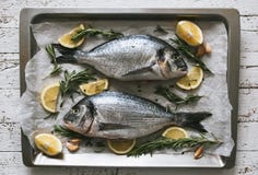 Pescados crudos frescos de la brema de Dorado o de mar con el limón y el romero foto de archivo libre de regalías Pescados crudos frescos de la brema de Dorado o de mar con el limón y el romero foto de archivo libre de regalías