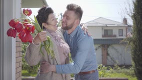 Petit-fils adulte rendant visite ? sa grand-m?re, apportant son bouquet des tulipes L'homme barbu ?treignant sa mamie Les gens banque de vidéos Petit-fils adulte rendant visite ? sa grand-m?re, apportant son bouquet des tulipes L'homme barbu ?treignant sa mamie Les gens banque de vidéos