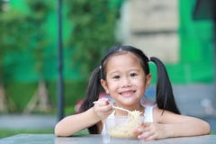 Petite fille asiatique adorable d'enfant mangeant les nouilles instantanées pendant le matin au jardin image libre de droits Petite fille asiatique adorable d'enfant mangeant les nouilles instantanées pendant le matin au jardin image libre de droits
