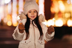 Petite fille de sourire mignonne avec des lumières de Bengale sur la rue le soir photo stock Petite fille de sourire mignonne avec des lumières de Bengale sur la rue le soir photo stock