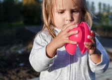 Petite fille jouant avec un coeur en plastique rouge elle le tient dans des ses mains Image stock Petite fille jouant avec un coeur en plastique rouge elle le tient dans des ses mains Image stock