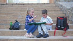 Petits camarades de classe avec des sacs à dos se reposant sur des étapes d'école et faire la critique du livre pendant la coupur banque de vidéos Petits camarades de classe avec des sacs à dos se reposant sur des étapes d'école et faire la critique du livre pendant la coupur banque de vidéos