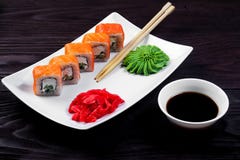 Petits pains de sushi de Philadelphie d'un plat carré blanc avec le wasabi, la sauce de soja et le gingembre Fond en bois foncé images libres de droits Petits pains de sushi de Philadelphie d'un plat carré blanc avec le wasabi, la sauce de soja et le gingembre Fond en bois foncé images libres de droits