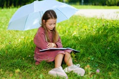 Peu fille dans le livre de lecture de robe en parc photographie stock libre de droits Peu fille dans le livre de lecture de robe en parc photographie stock libre de droits