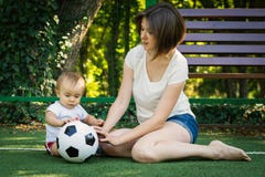 Peu garçon regardant le ballon de football et l'explorant se reposant à côté de la mère au terrain de football Fils d'enfant en b photos stock Peu garçon regardant le ballon de football et l'explorant se reposant à côté de la mère au terrain de football Fils d'enfant en b photos stock