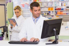 Pharmacien de sourire à l'aide de l'ordinateur photographie stock Pharmacien de sourire à l'aide de l'ordinateur photographie stock