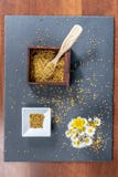 Photo composed of a square bowl of white ceramic, a wooden box full of pollen grains of bees and a bunch of daisies, on a slate stock photo Photo composed of a square bowl of white ceramic, a wooden box full of pollen grains of bees and a bunch of daisies, on a slate stock photo