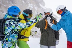 Photo of four happy snowboarders in helmet doing handshake on mountains background .