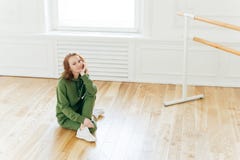 Photo of professional female dancer has rest after training, poses on floor near ballet barre, has ballet classes, wears green royalty free stock image Photo of professional female dancer has rest after training, poses on floor near ballet barre, has ballet classes, wears green royalty free stock image