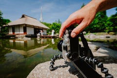 Photograph Male Hand Handling An Old Vintage Camera On Tripod In Front Of Water Pond With Landmark Japanese House And Stock Images Photograph Male Hand Handling An Old Vintage Camera On Tripod In Front Of Water Pond With Landmark Japanese House And Stock Images