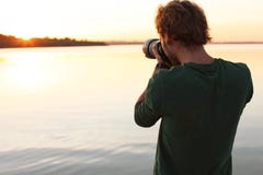 Photographe masculin prenant la photo du coucher du soleil de rive avec l'appareil-photo professionnel photographie stock libre de droits Photographe masculin prenant la photo du coucher du soleil de rive avec l'appareil-photo professionnel photographie stock libre de droits